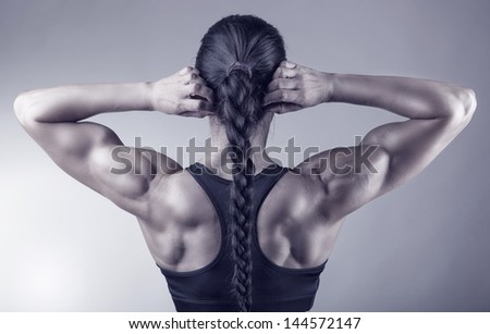 Athletic young woman showing muscles of the back and hands on a gray background
