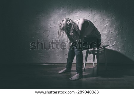 Young sad woman sitting alone in a chair in an empty room