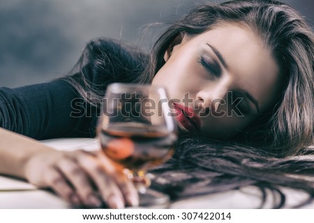 Young beautiful woman drinking alcohol on dark background. Focus on woman