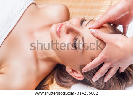 Beautiful young woman receiving facial massage with closed eyes in a spa salon