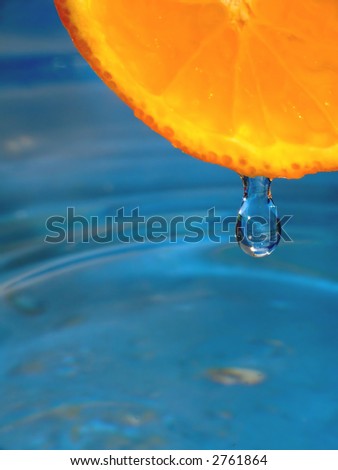 A nice and fresh close-up of a drop hanging from a orange. Blue background
