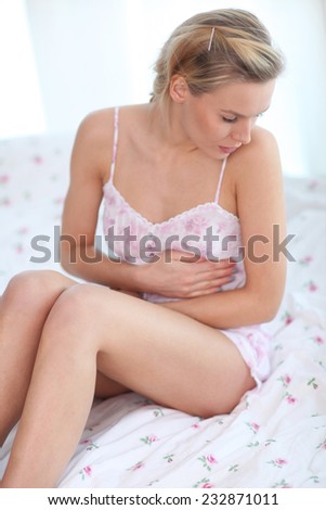 Young woman with stomach ache sitting on bed. Stomachache