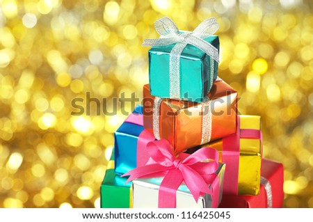 Pile of small gifts on gold blurry lights background.(horizontal) Many gifts wrapped colorful metallic paper and ribbon.