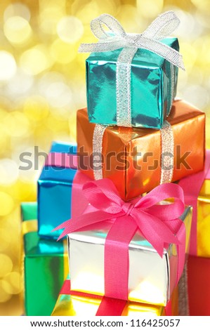Pile of small gifts on gold blurry lights background.(vertical) Many gifts wrapped colorful metallic paper and ribbon.