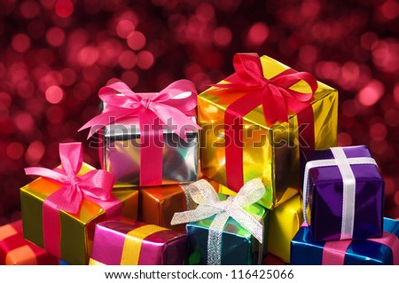 Pile of small gifts on red blurry lights background. Many gifts wrapped colorful metallic paper and ribbon.