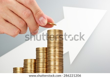 Putting coins with growing arrow. Building your assets. Hand putting 500 yen coins and building coin graph with upside growing arrow. White reflection background.