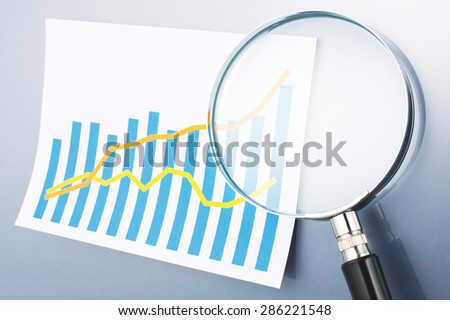 Graph and magnifying glass on gray background. Reading data. Looking graph with magnifying glass. Calculating, graphing and analyzing data.