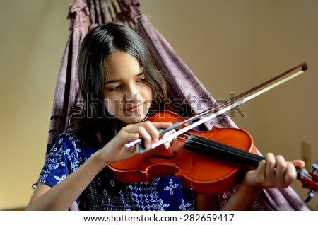 Little Hispanic girl plays the violin in a hammock on a sunny afternoon