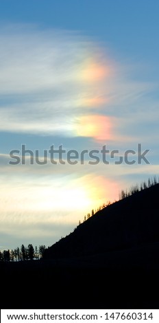 Neat sundog over silhouetted mountains with fluffy white clouds. Yellowstone National Park, USA