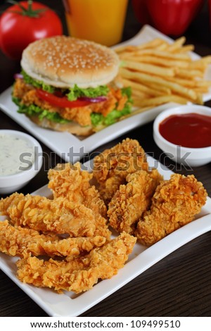 Full plate of crispy chicken sticks , burger and french fries.