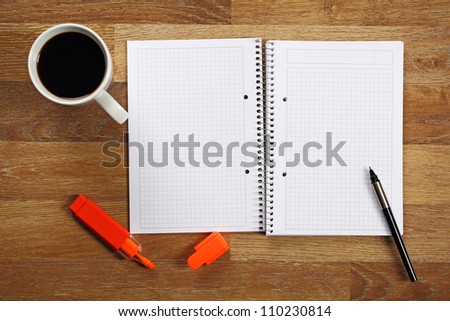 Opened notebook, cup of coffee and pen on wooden office desk.
