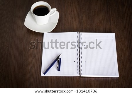 Opened notebook, pen and cup of coffee on dark wooden office desk.