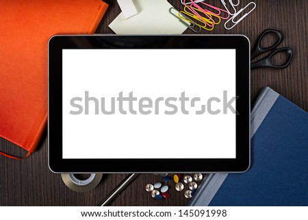 Top view on dark wooden office desk with office equipment in chaos and digital tablet with blank screen on top of it.