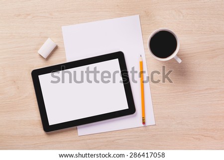 Office equipment such as digital tablet, notebook with pencil and coffee mug on wooden office desk.