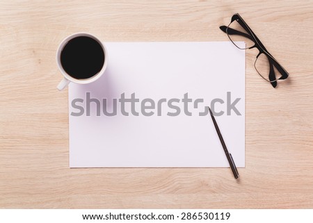 Empty sheet of paper, mug of black coffee, glasses and pen od light wooden office desk.
