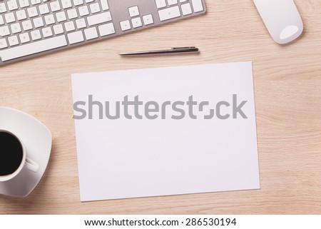 Office equipment such as computer keyboard, mouse, sheet of paper and pen on office wooden desk with coffee.