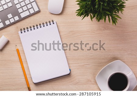 Notepad, pencil, white computer keyboard, mouse, plant and cup of coffee on wooden office desk.