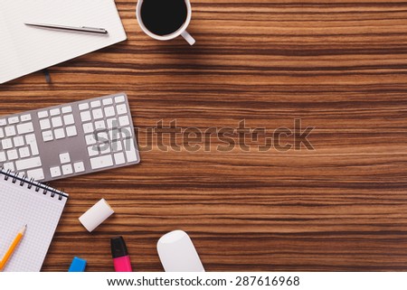 Empty space next to office equipment such as computer modern keyboard, white mouse, notepad, pencil, mug of coffee and other office equipment on dark wooden office desk.