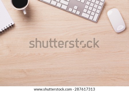 Empty space next to office equipment such as computer modern keyboard, white mouse, notepad, pencil and mug of coffee on bright wooden office desk.