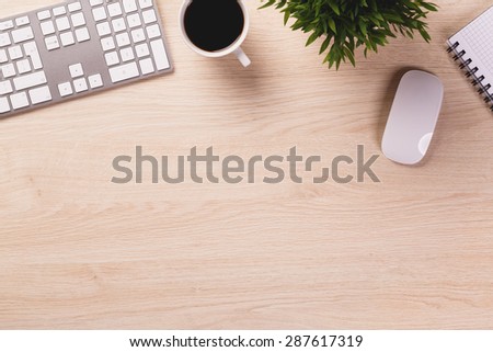 Empty space next to office equipment such as computer modern keyboard, white mouse, notepad, mug of coffee and plant on bright wooden office desk.
