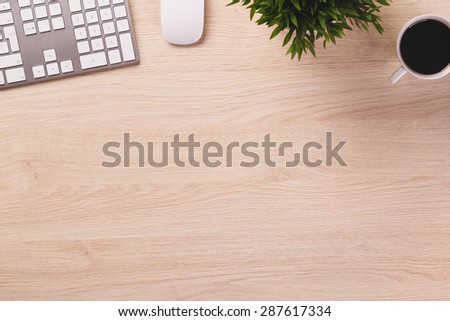 Empty space next to office equipment such as computer modern keyboard, white mouse, mug of coffee and plant on bright wooden office desk.