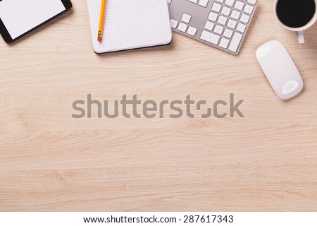 Empty space next to office equipment such as computer modern keyboard, white mouse, notepad, pencil, mug of coffee and digital tablet on bright wooden office desk.
