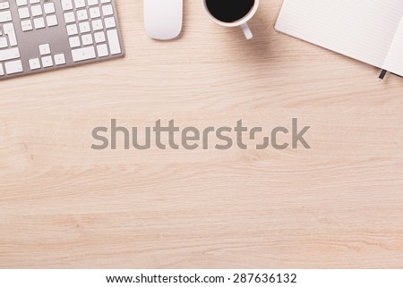 Empty space next to office equipment such as computer modern keyboard, white mouse, notepad and mug of coffee on bright wooden office desk.