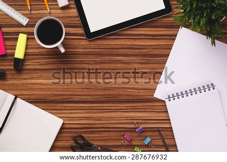 Empty space in the middle of office equipment such as digital tablet, notepad, sheet of paper, notebook, highlighter, ruler, plant and other on dark wooden office desk.