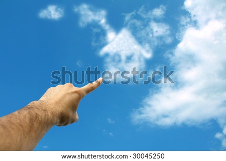 Adult finger pointing at house formed from clouds in sky.