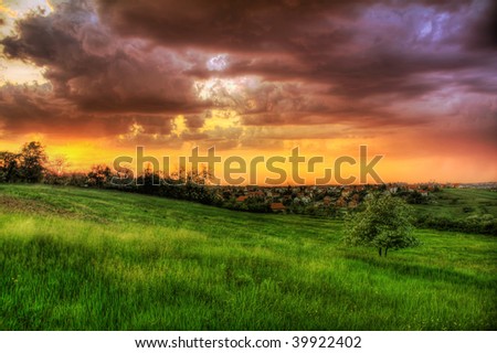 Colorful sunset over  countryside fields with village in background.
