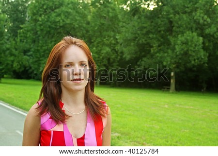 A portrait of a pretty girl in bright pink and red outfit walking in a park.
