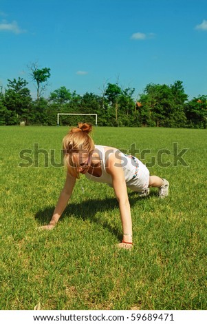 Young woman performing push-up or press-up exercise on soccer field.