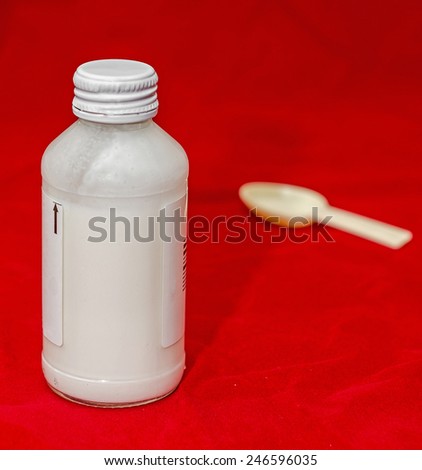 White bottle with medical drug syrup and a small spoon, red background
