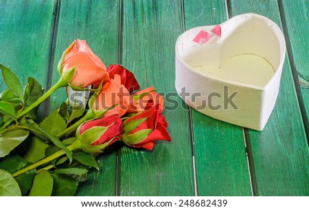 Red and orange roses flower with heart shape gift box, green wood background.