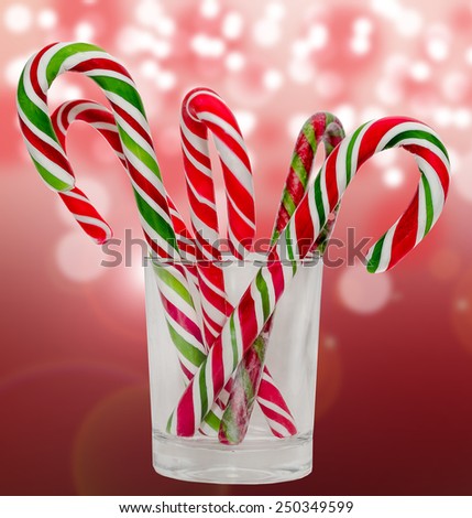 Colored candy sticks and Christmas lollipops in a transparent glass, red bokeh background.
