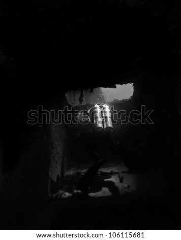A technical diver in complete darkness outlined by a open doorway creating a shadow in a sunken shipwreck in the John Pennekamp State Park. The USCG Bibb in Key Largo, Florida.