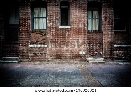 A brick alleyway with concrete walkway. Old windows and doors made of metal and glass with stairs and steps