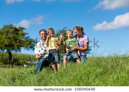 Family with two little boys playing in the grass on a summer meadow - they have a football