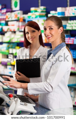 Pharmacist with female assistant in pharmacy standing at the cashpoint