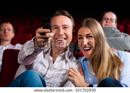 Couple and other people, probably friends, in cinema watching a movie, they try to switch to another program that is not possible in a cinema