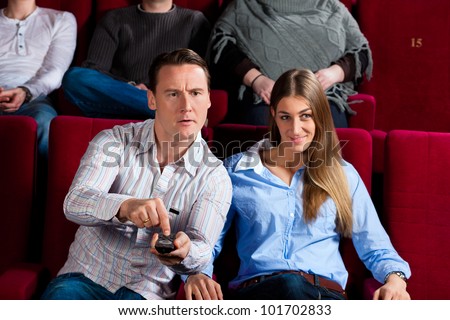 Couple and other people, probably friends, in cinema watching a movie, they try to switch to another program that is not possible in a cinema
