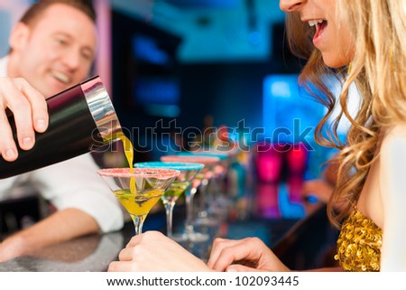 Young people in club or bar drinking cocktails and having fun; the barkeeper is mixing drinks