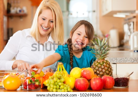 Healthy eating - mother and child sitting in the kitchen with different kinds of fruits for breakfast food