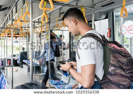 Young male tourist with a big backpack using the mobile phone for guidance or communication while standing in the bus in Jakarta