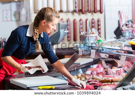 Sales woman in butcher shop putting different kinds of meat and sausage in display