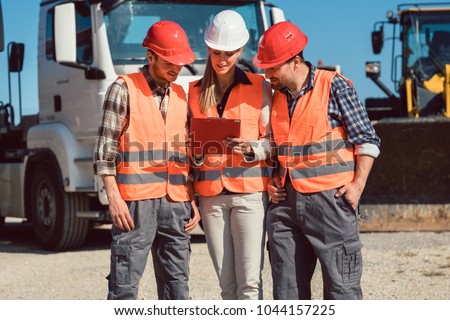 truck drivers and dispatcher in front of lorries in freight forwarding company looking at tablet computer