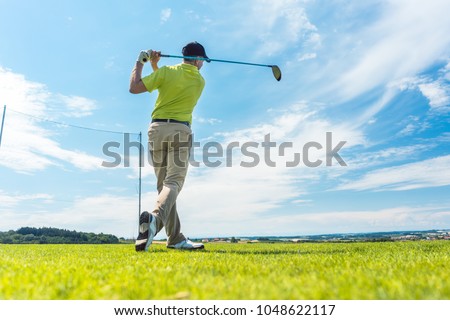 Full length rear view of a man holding the club in the finish position of a driving swing, while playing golf during individual game outdoors on a professional ground