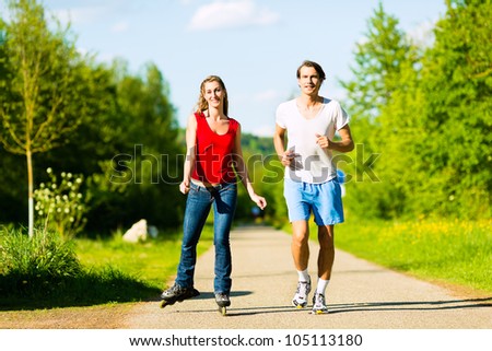 Young couple - man and woman - doing sports outdoors, he is jogging while she is roller blading