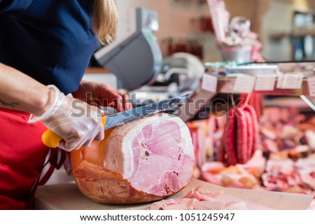 Experienced butcher shop assistant cutting ham to sell it