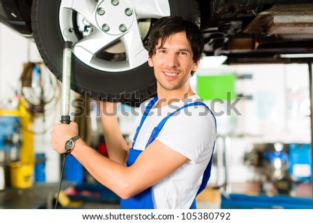 Young man in blue overall - mechanic - working with lamp on jacked car in a service station